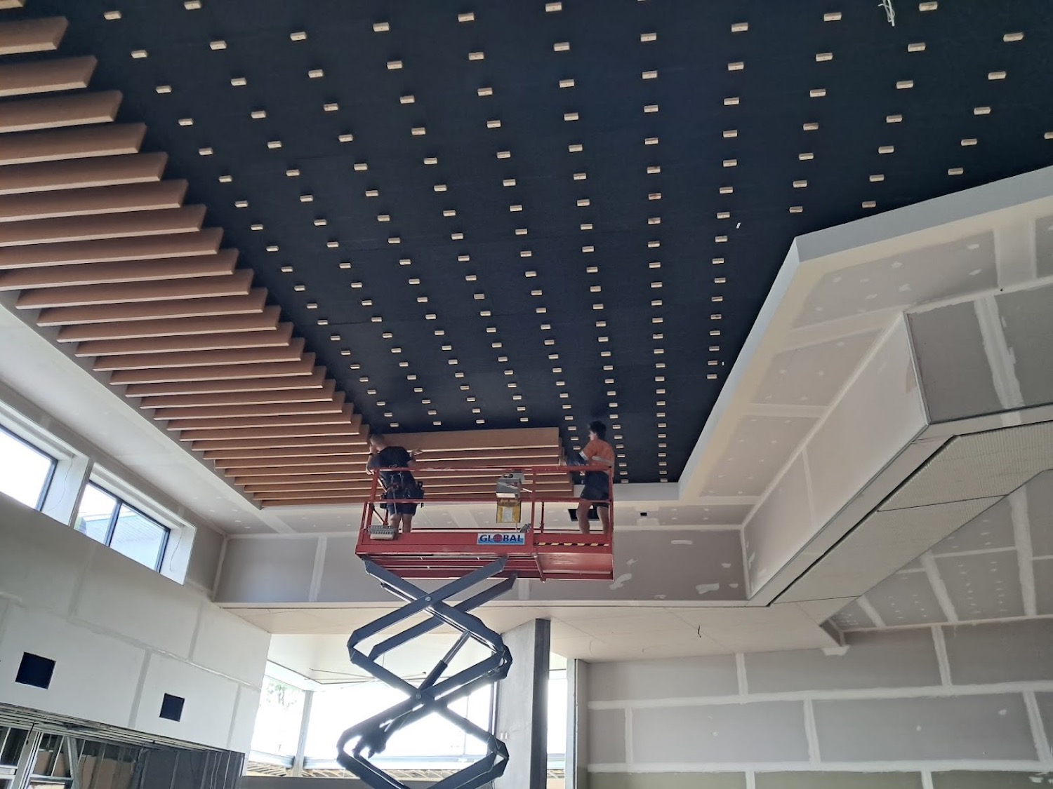 Two workers on a scissor lift fixing a battened ceiling