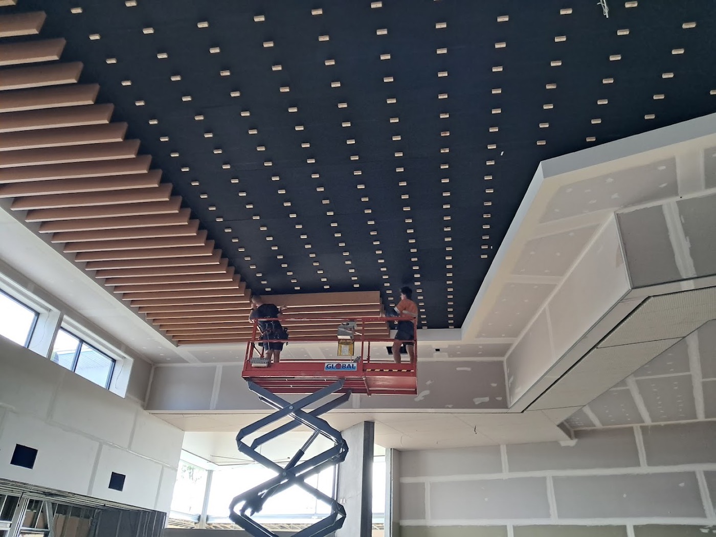A dark slatted timber ceiling with recessed downlights being installed above a plasterboard fit-out